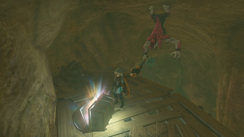 Zelda: TotK screenshot - Link opening a chest in the gave, while a horriblin hangs from the ceiling behind him.